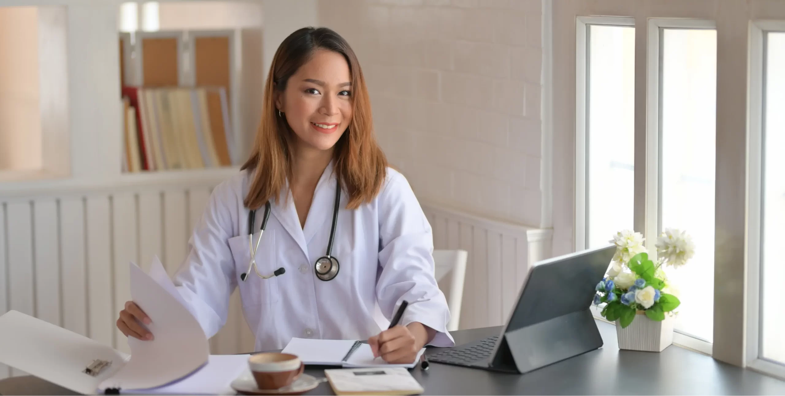 young-female-doctor-working-with-tablet-writing-paperwork-office-room-1-scaled.webp